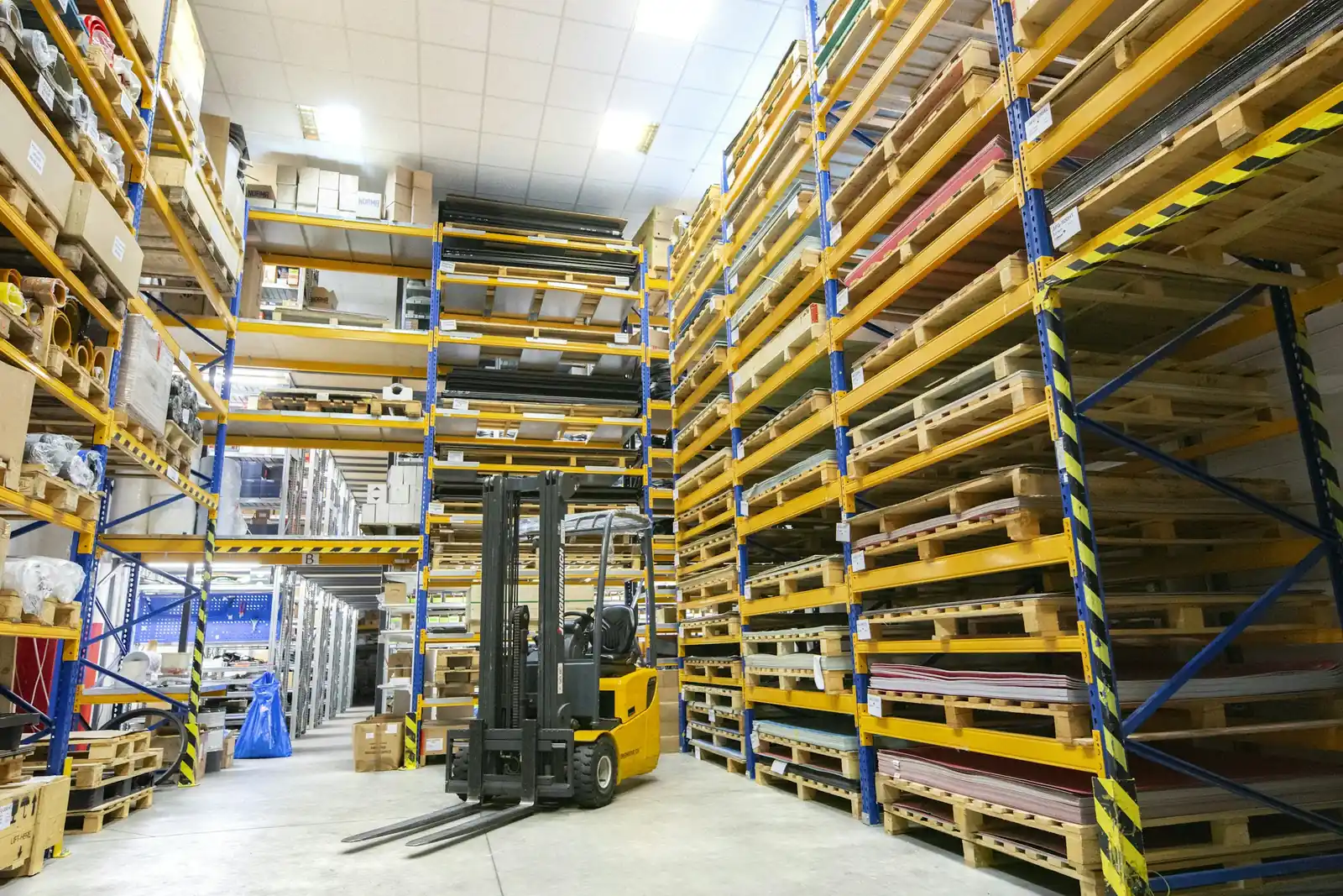 Tall pallet racking stacked with timber pallets in a working warehouse, with a forklift in the aisle.