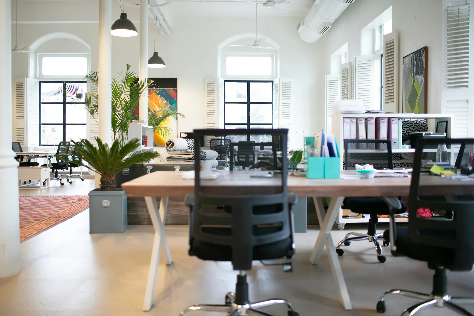 Louvred shutters and arched windows stand behind a timber bench desk on white X-frames.