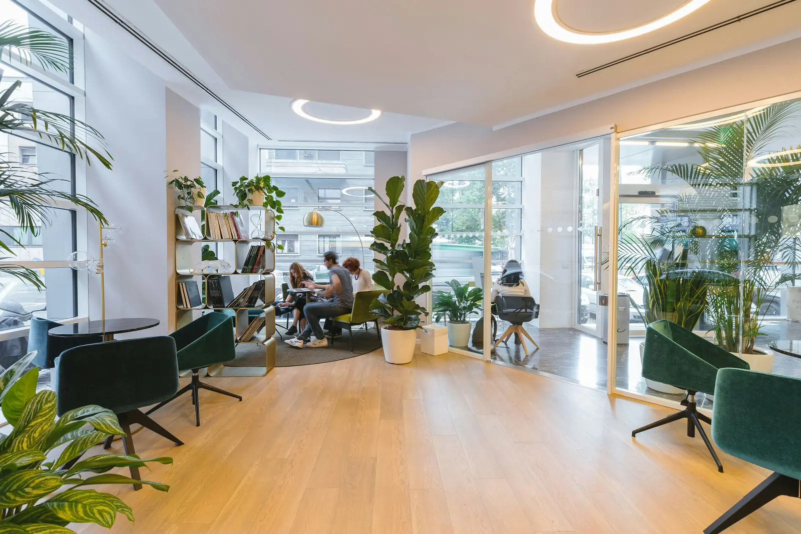 Three people work at the window while green velvet swivel chairs sit empty on pale floorboards.