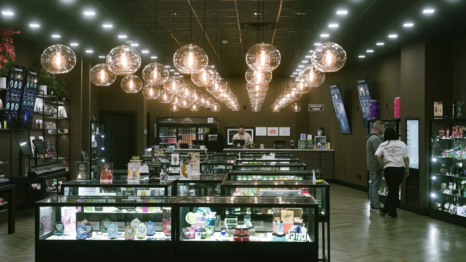 Lit glass display cabinets run down a herringbone timber floor, clustered globe pendants above.