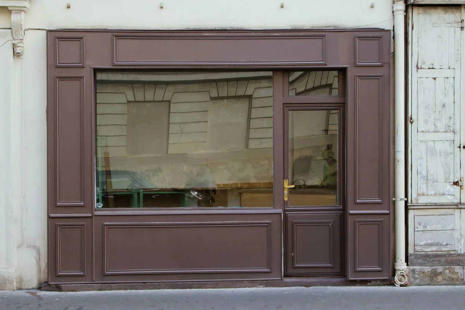 Behind the glass of a freshly painted brown panelled shopfront, the unit is stripped to bare plaster.
