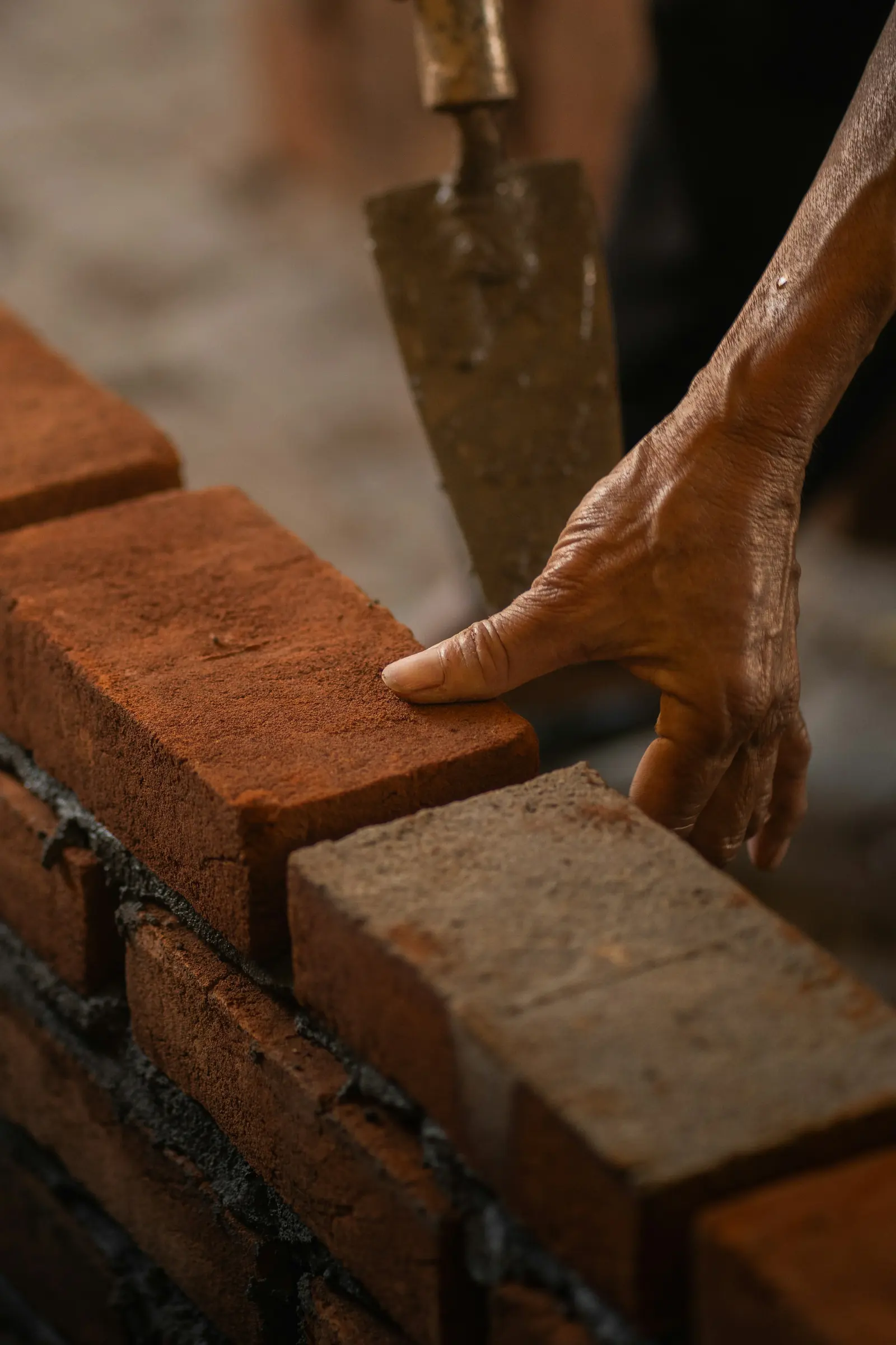 Hands laying a brick onto a mortar bed against a string line.
