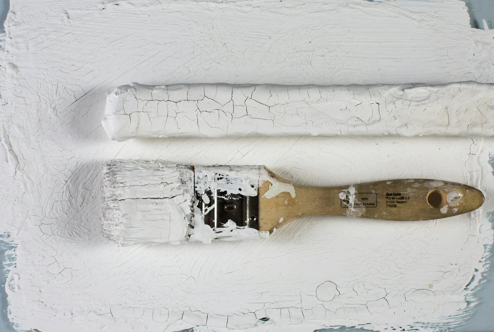 Laid flat on crazed white paintwork, a brush sits clogged solid to the ferrule.