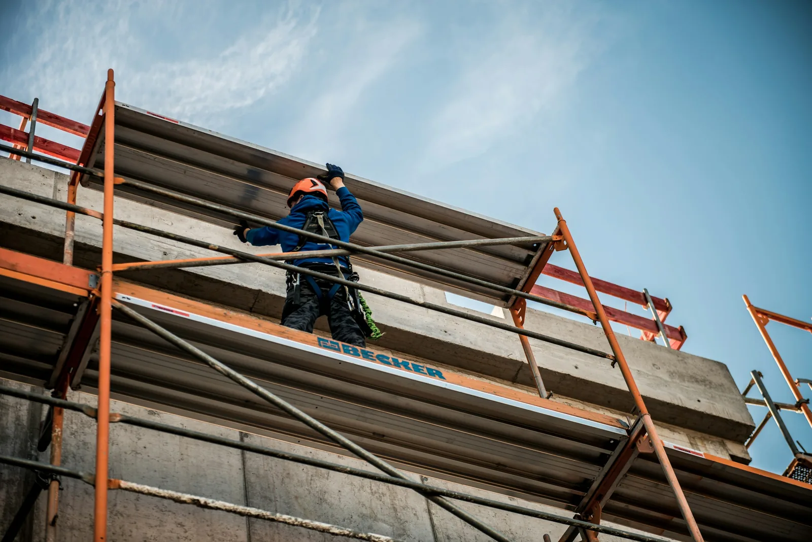 A worker in a safety harness sets a ribbed metal edge panel against the concrete slab.