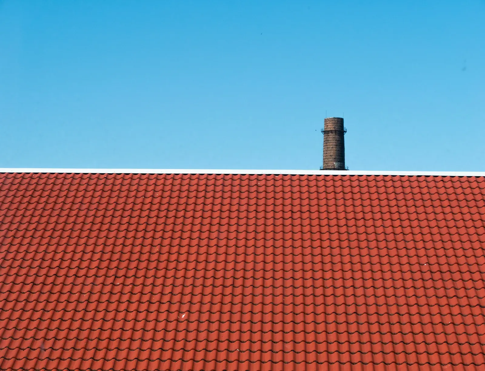 Behind the white ridge flashing of a red pantile roof stands a round industrial chimney.