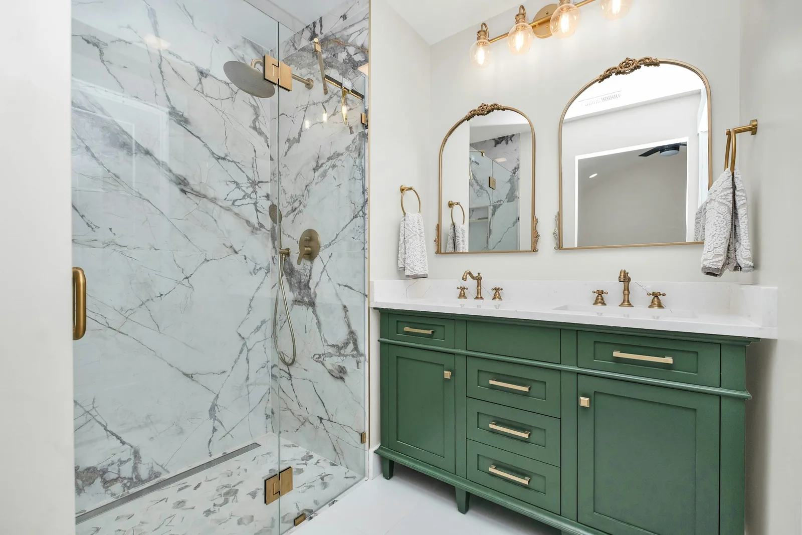 A bathroom with green cabinets and a marble shower enclosure.