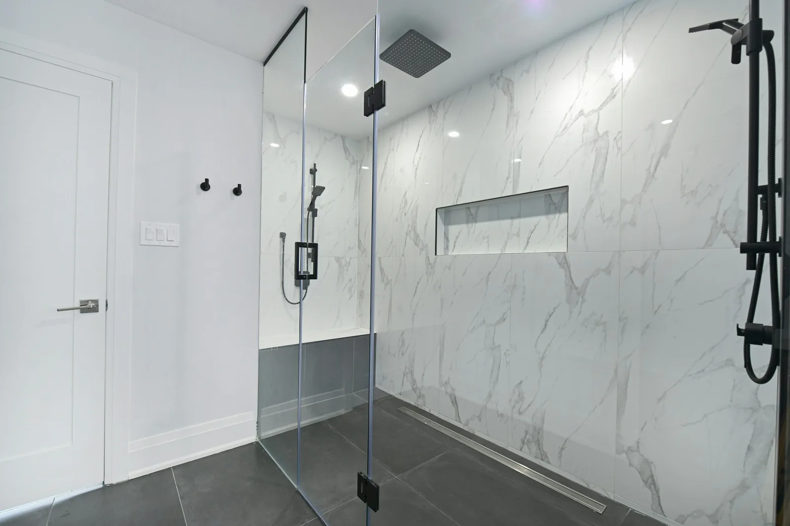 A glass-enclosed shower with marble walls.