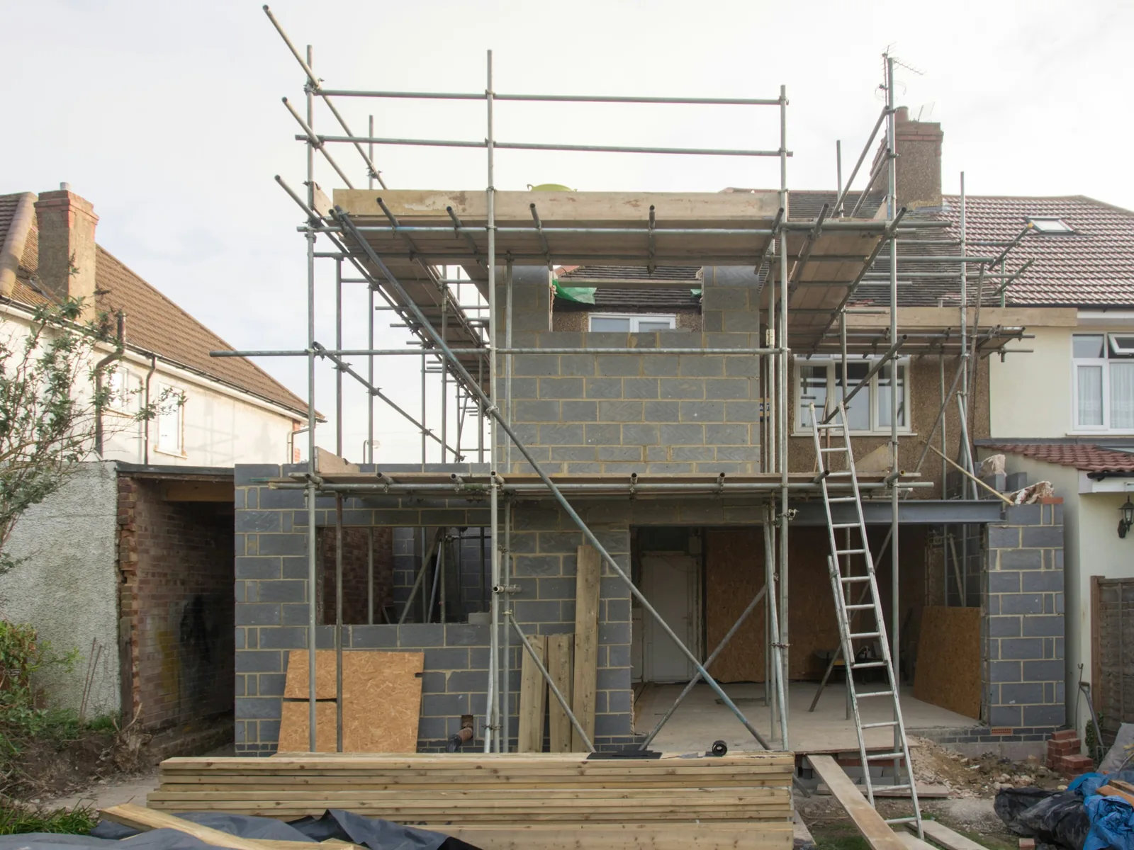Scaffold wraps a bare blockwork shell two storeys high, no roof on it yet.