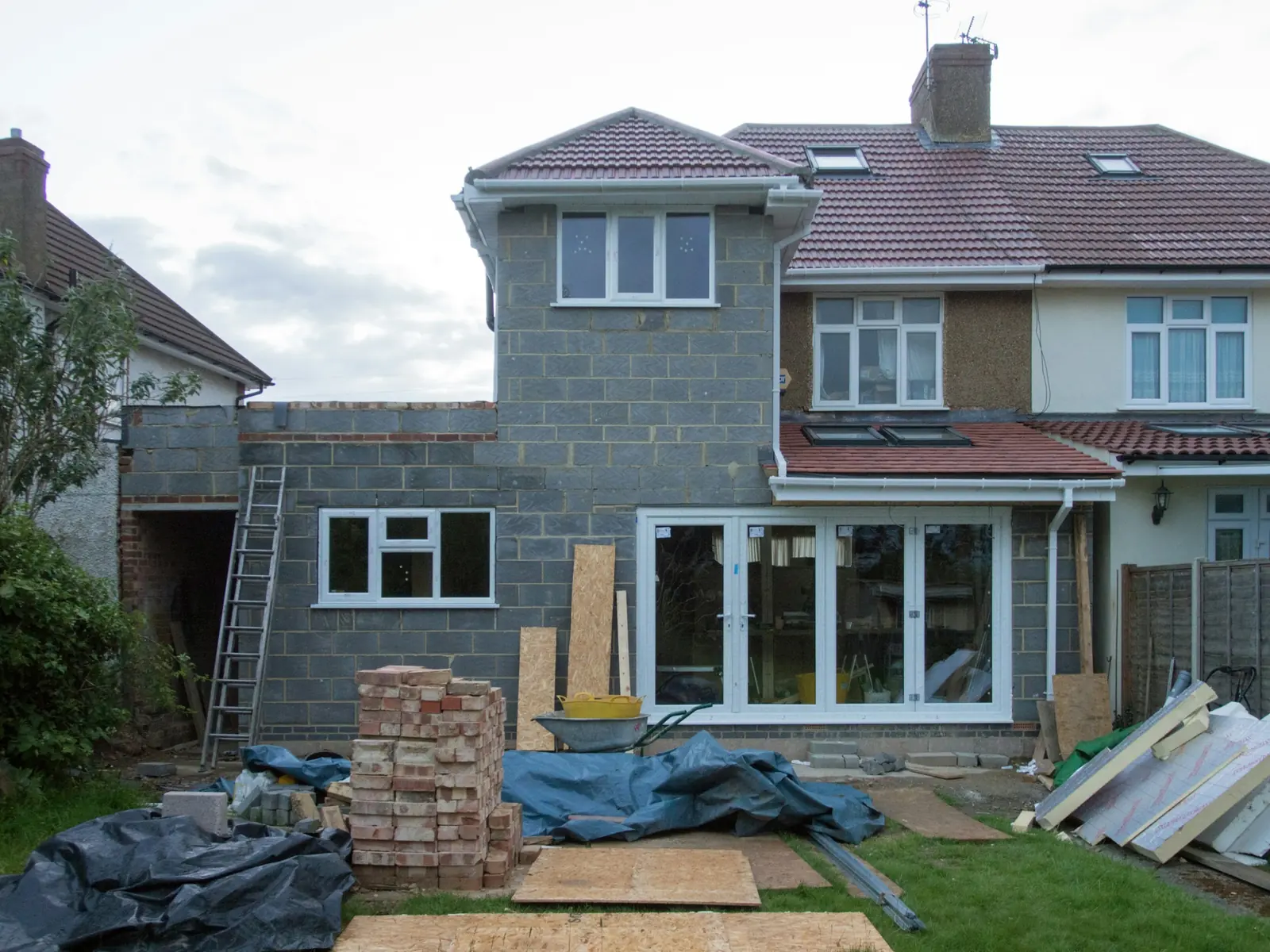 Roof tiled and doors hung, the blockwork still bare, insulation boards leaning against the fence.