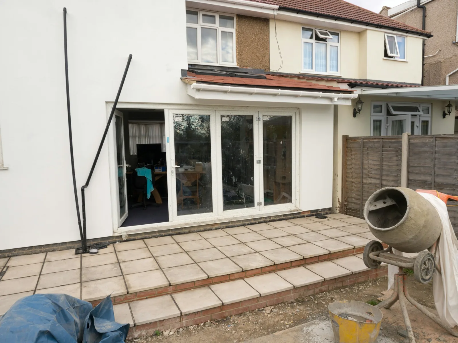 One French door standing open onto the paved patio, the cement mixer parked alongside.