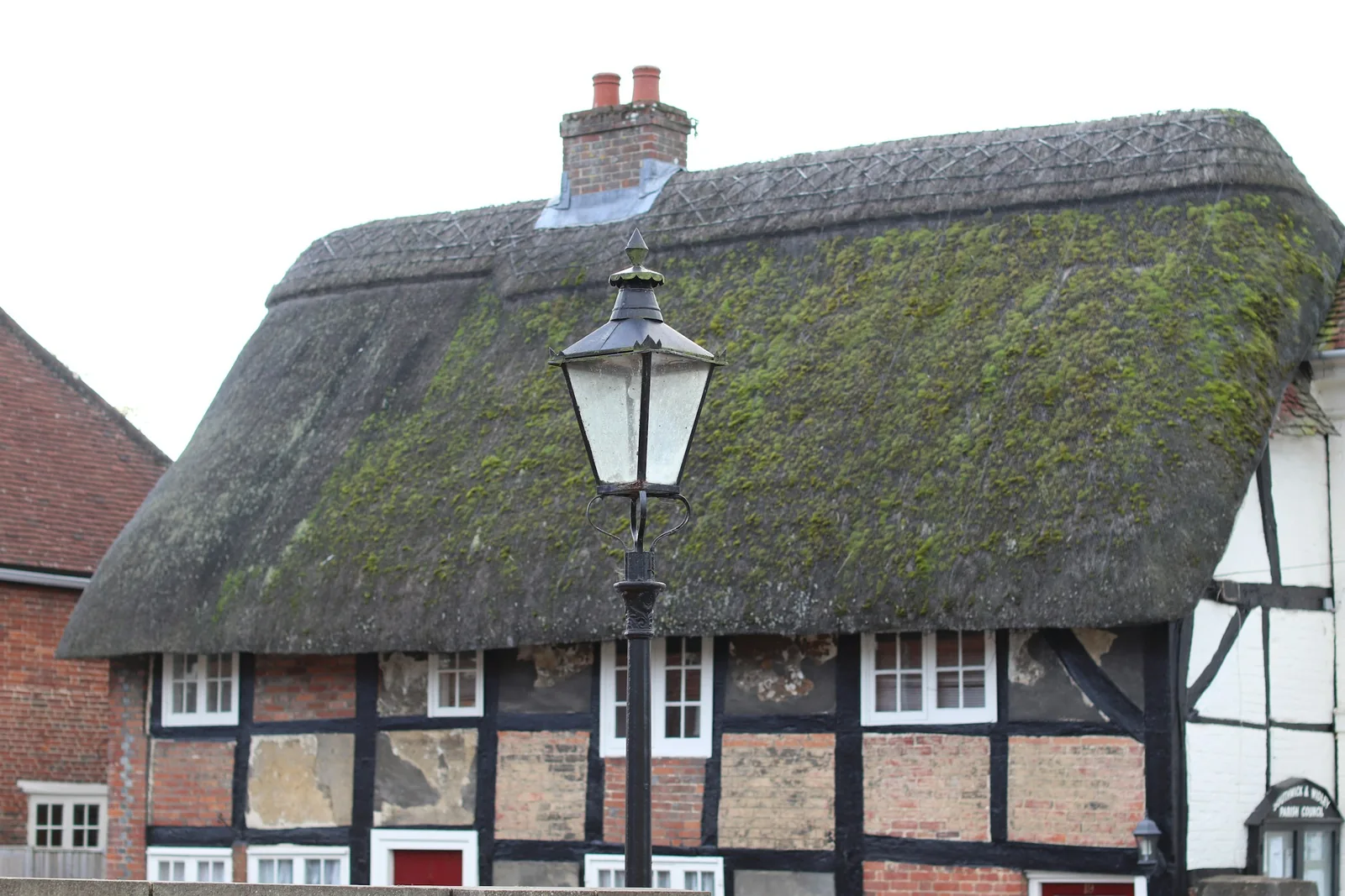A thatched cottage behind a lamppost.