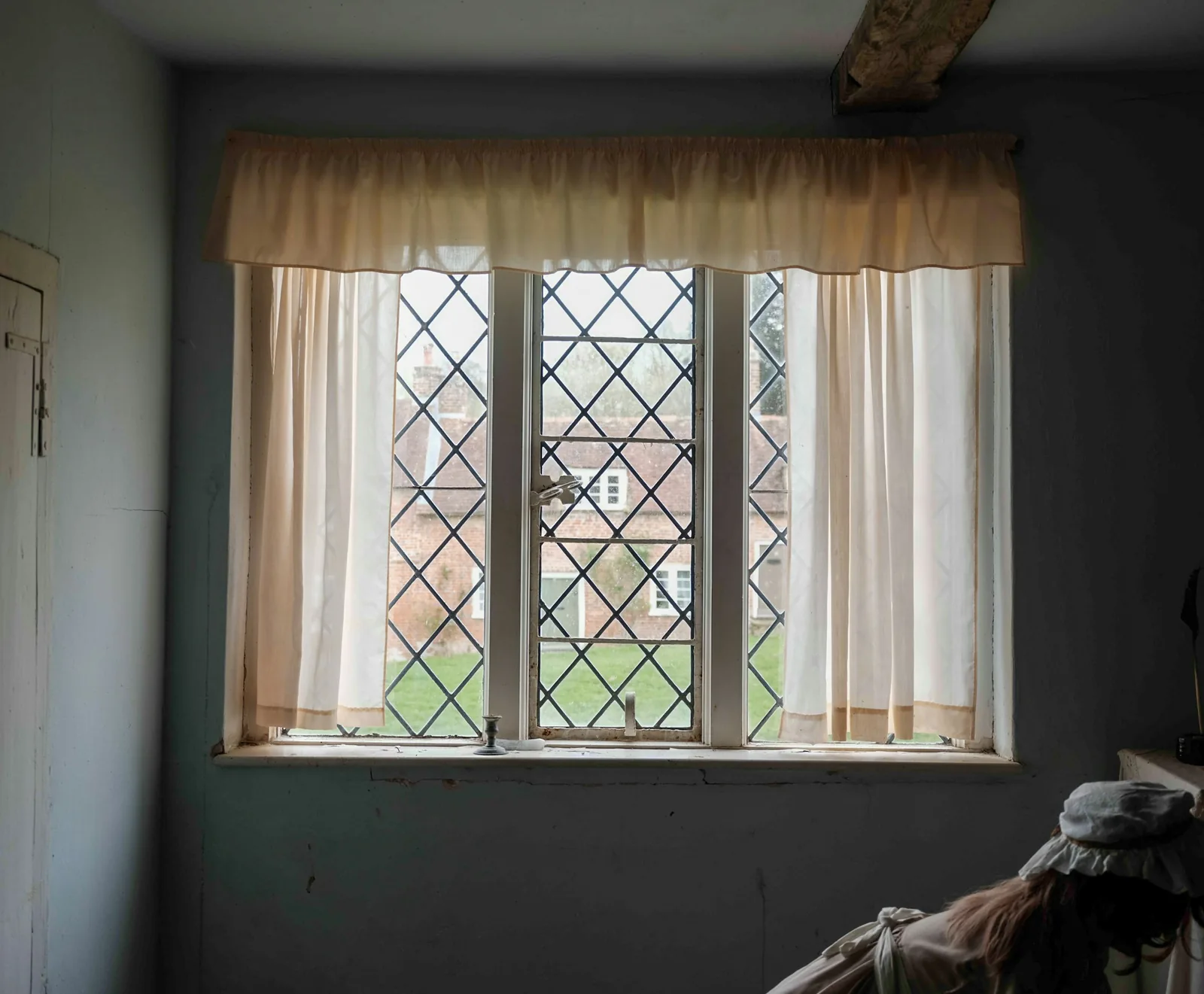 A leaded period window with curtains, lit by daylight.