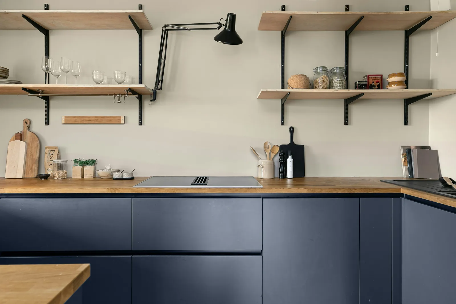 A kitchen with navy blue base units, a timber worktop and open shelving.