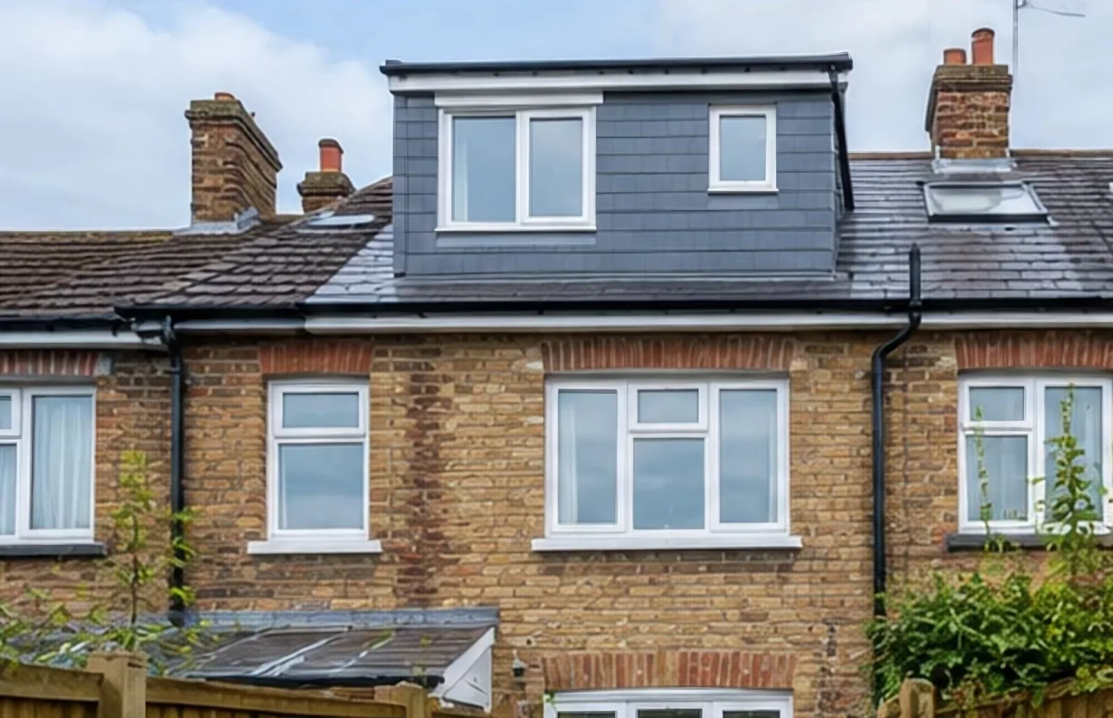 A slate-hung dormer with white windows on the rear roof of a yellow-brick terraced house.