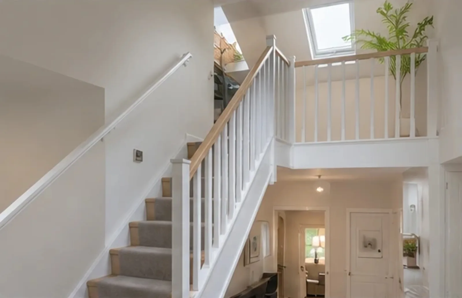 A new staircase with white balustrades rising to a converted loft lit by a roof window.