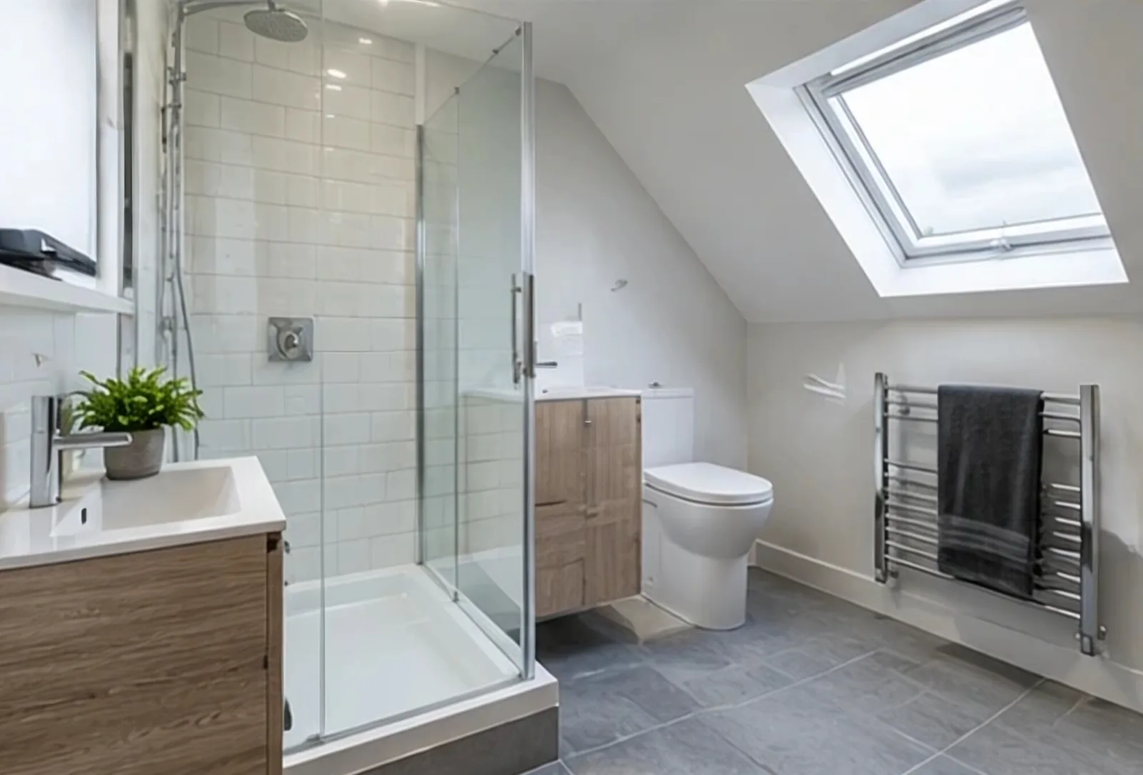 A loft shower room with a glass enclosure, white tiles, a heated towel rail and a roof window.