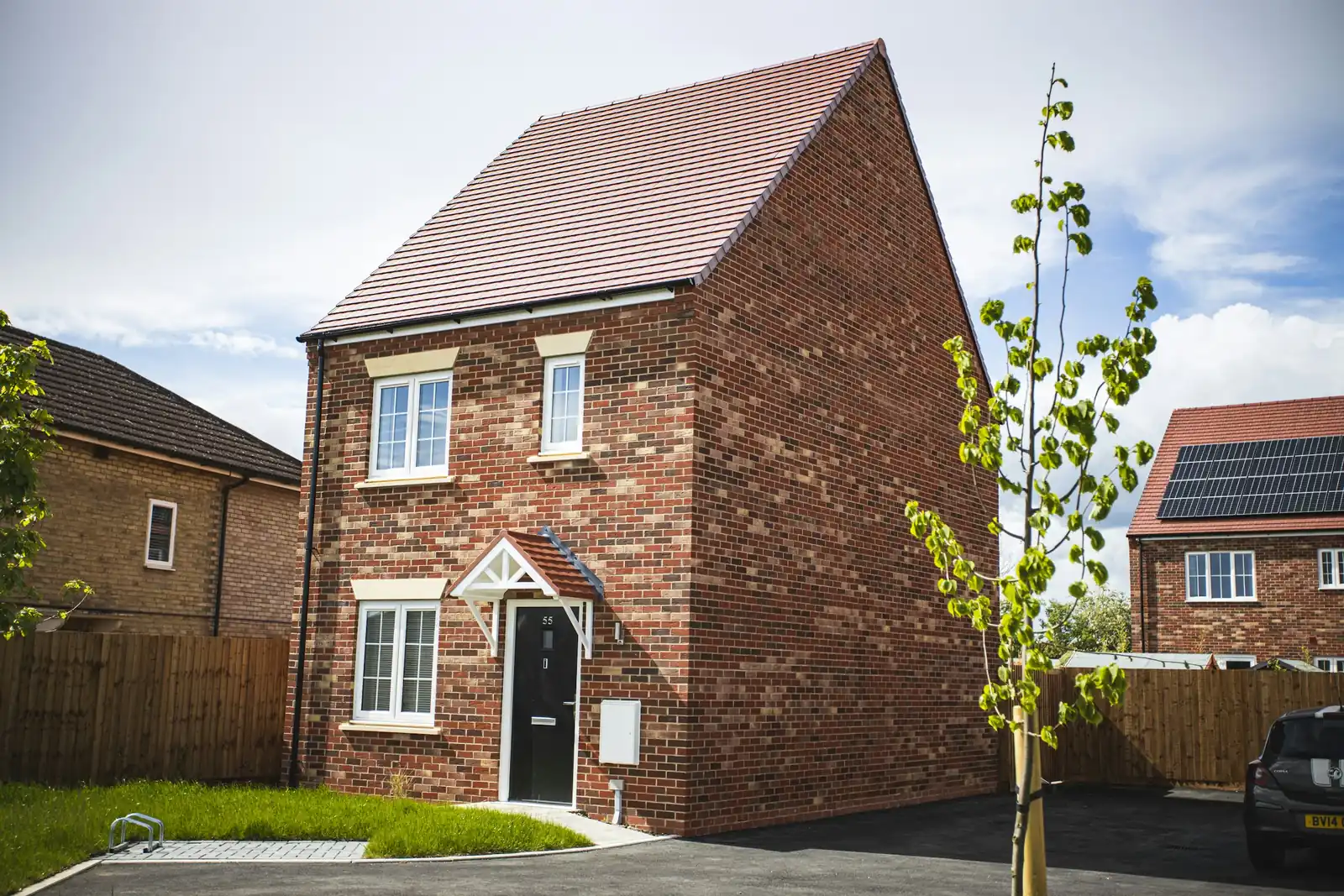 Timber brackets hold a tiled canopy over the black front door; the gable end beside it is blank brick.